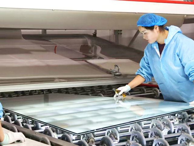 Worker inspecting glass panel on automatic washing and inspection line